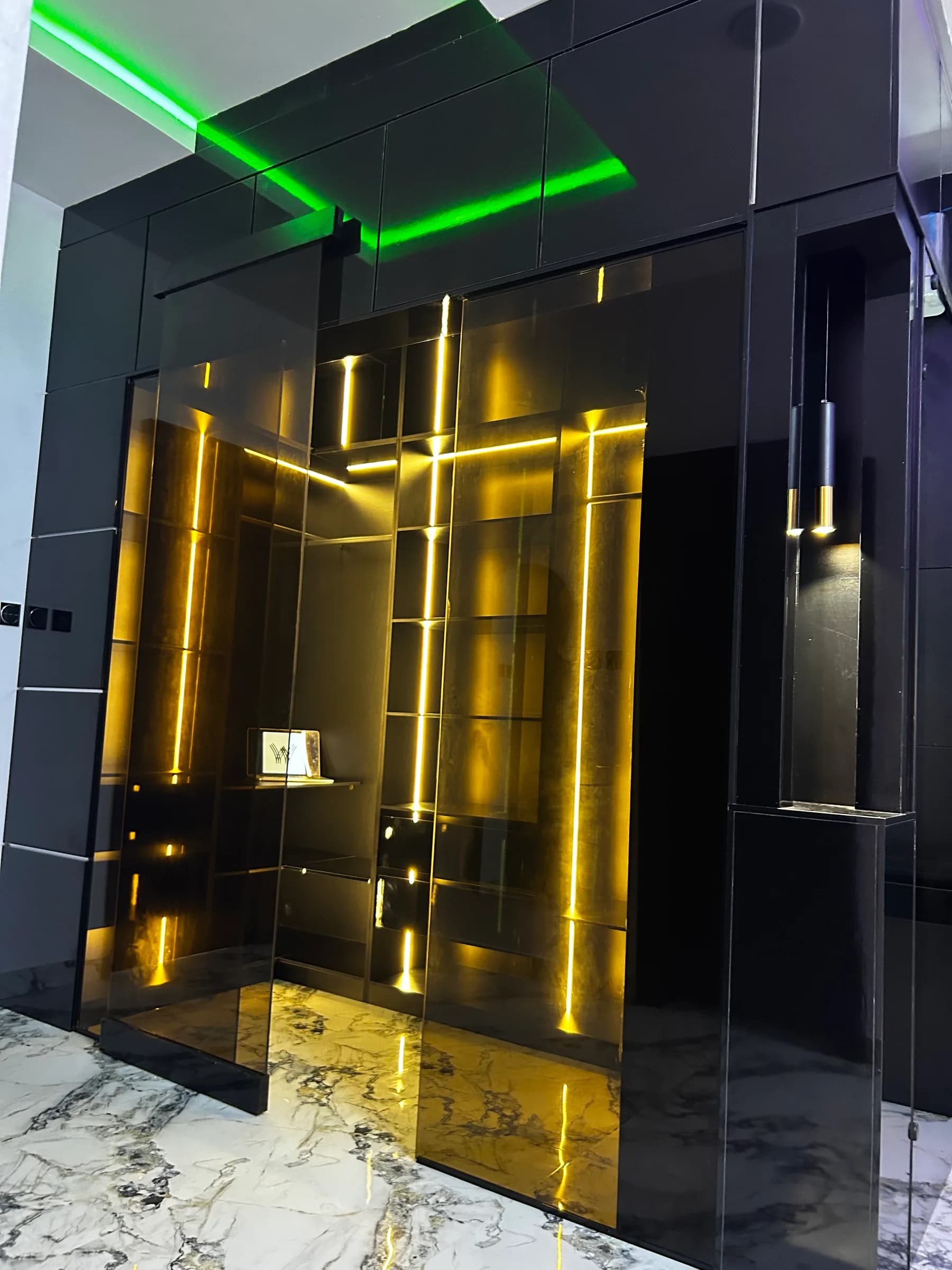 Brass and smoked-glass wardrobe run lit from within, against black gloss panelling.
