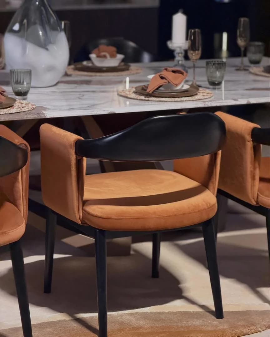 Tan velvet dining armchair with a curved black backrest at a styled marble dining table.