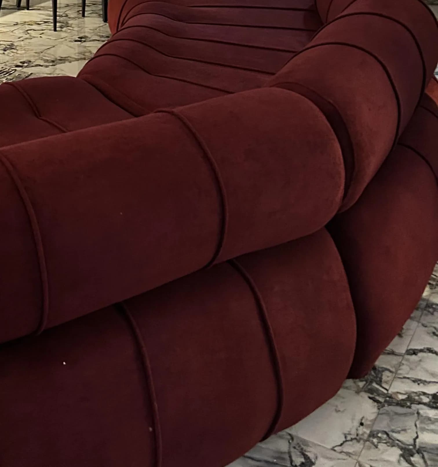 The full curve of the burgundy Helix sofa between a timber plank door, a lit bar and a brass coffee table.