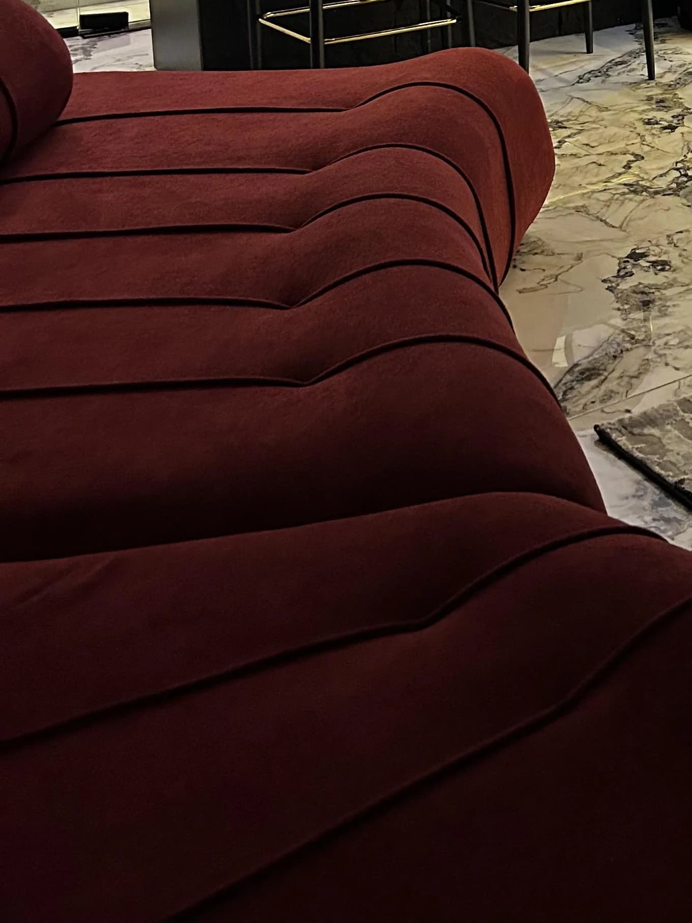 The full curve of the burgundy Helix sofa between a timber plank door, a lit bar and a brass coffee table.