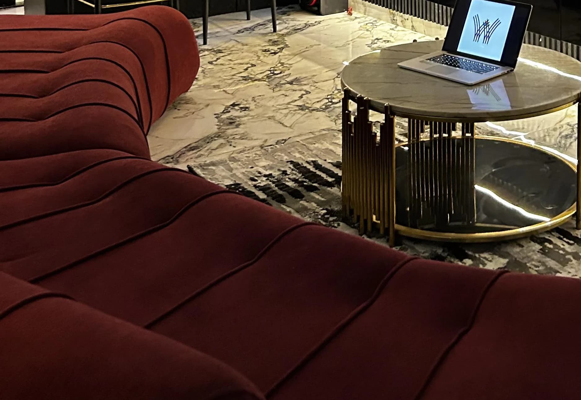 The channelled burgundy seat of the Helix beside a brass and marble coffee table.