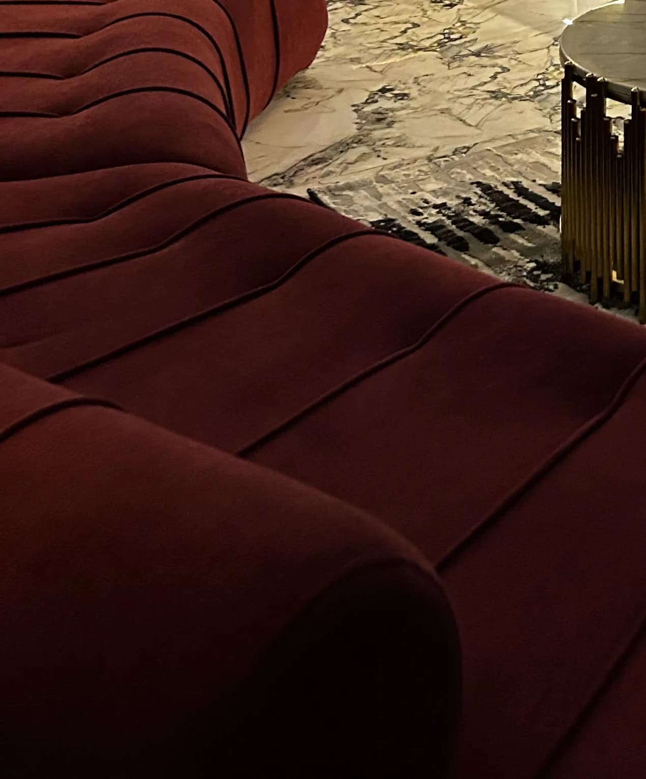 The full curve of the burgundy Helix sofa between a timber plank door, a lit bar and a brass coffee table.