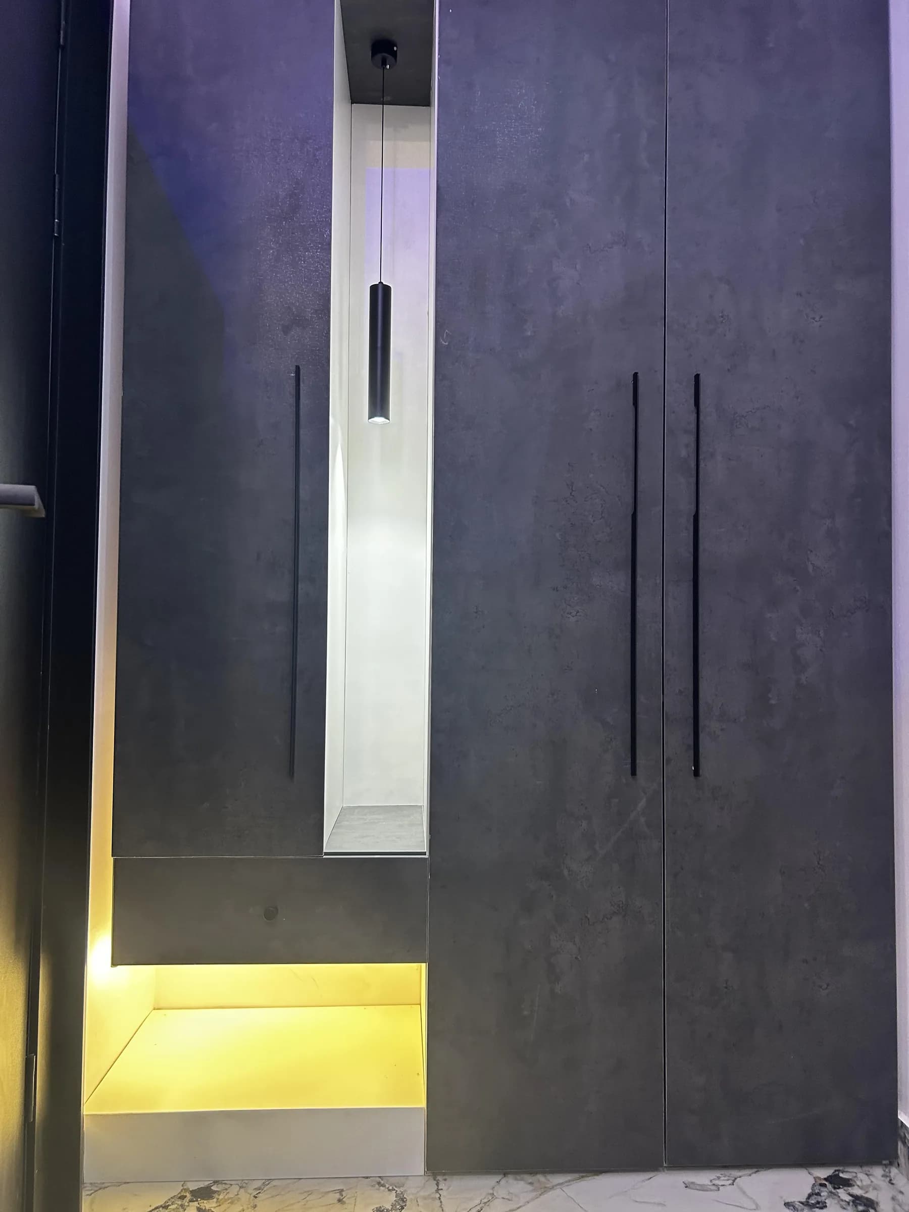 Concrete-effect wardrobe with a pendant-lit niche and a glowing open base.